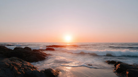 A breathtaking view of the sun setting over gentle waves crashing on rocks, highlighting the calm beauty of nature and the peaceful shoreline atmosphere.の素材