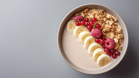 A visually appealing healthy breakfast bowl featuring sliced bananas, vibrant berries, crunchy granola, and creamy yogurt arranged on a gray surface.の素材