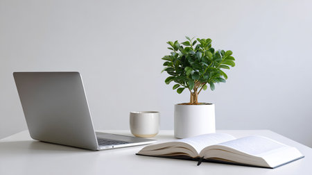 A modern workspace featuring a sleek laptop, an open book, a stylish coffee mug, and a vibrant potted plant, all arranged on a pristine white desk to inspire productivity.の素材
