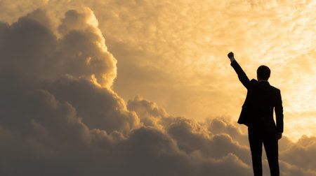 A silhouette of a businessman in a suit raises his fist against a stunning sunset, embodying themes of triumph, ambition, and motivation in the workplace.の素材