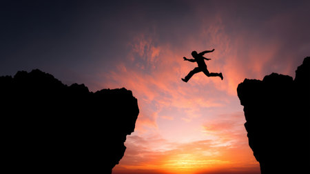 A silhouette of a person leaping between two rocky cliffs at sunset, symbolizing courage and adventure in nature, creating a dramatic and inspiring scene.の素材