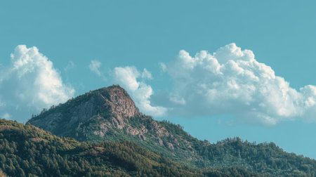 This stunning mountain landscape features a vibrant blue sky and fluffy clouds, complemented by a lush green forest below, perfect for nature enthusiasts and travelers.の素材