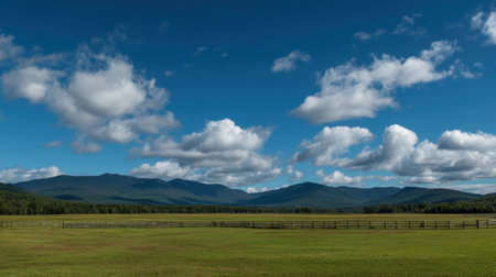 A serene meadow stretches across the scene, framed by majestic rolling hills. Fluffy clouds drift in a blue sky, creating a tranquil atmosphere perfect for nature lovers.の素材