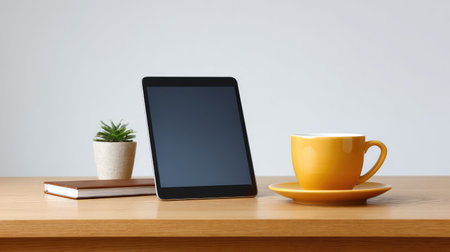 A stylish modern workspace featuring a tablet, a vibrant yellow cup of coffee, a notepad, and a small green plant on a sleek wooden desk, ideal for inspiration and productivity.の素材