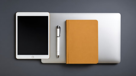 A clean and modern workspace setup featuring a tablet, laptop, notebook, and pen on a grey background, perfect for showcasing creativity and productivity in professional environments.の素材
