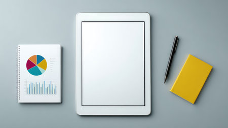 A modern workspace arrangement featuring a tablet, a notebook with a pie chart, and a pen on a flat surface, perfect for planning and productivity efforts.の素材