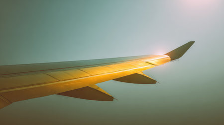 A stunning perspective of an airplane wing soaring through blue skies, adorned in golden sunlight, perfect for showcasing travel, aviation, and adventure themes.の素材