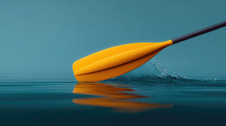 A stunning close-up of a yellow kayak paddle creates gentle ripples on the tranquil blue water surface, illustrating the serene beauty of outdoor recreation and adventure.の素材