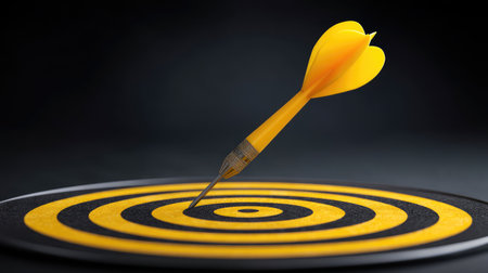 A bright yellow dart piercing the center of a circular black and yellow target highlights the essence of focus and precision in achieving goals and success.の素材