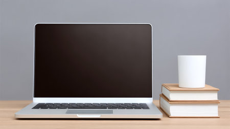 A minimalist workspace featuring a sleek laptop with a blank screen, stacked books, and a white cup, perfect for representing productivity and creative thoughts.の素材