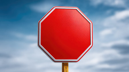 A vibrant red stop sign stands prominently against a backdrop of cloudy blue sky, symbolizing traffic regulations and enhancing urban safety themes for various applications.の素材