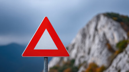 A striking triangular warning sign stands out against a blurred rocky backdrop, highlighting the theme of caution and safety in nature, perfect for travel and road safety themes.の素材