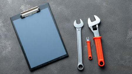 A set of red and silver tools is positioned next to a blank clipboard on a textured gray surface, ideal for showcasing repair and maintenance themes in various projects.の素材