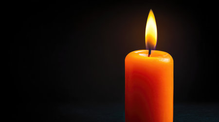 A vibrant orange candle burns with a steady flame, casting a warm glow against a dark background, perfect for creating a serene and peaceful mood in any setting.の素材