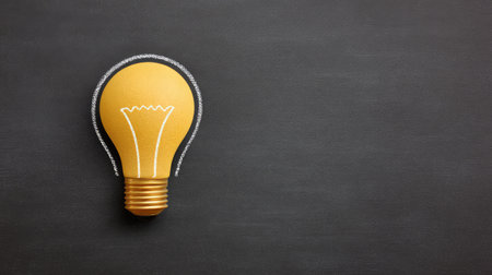 A vivid yellow light bulb illustration set against a dark chalkboard background, representing innovation and creativity in education and business fields.の素材