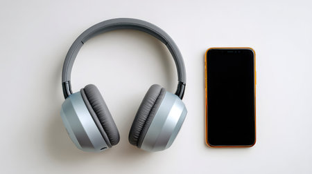 A sleek pair of stylish wireless headphones sits next to a modern smartphone on a clean white surface, representing audio technology and minimalistic design for music lovers.の素材