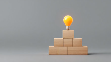 A minimalist arrangement of wooden blocks creating a foundation topped with a glowing light bulb, representing innovative thinking and the process of idea generation in a modern workspace.の素材