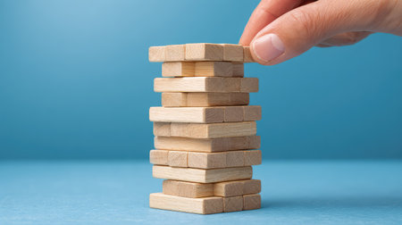 A close-up view of a hand placing a wooden block on a tower, illustrating themes of strategy and balance within a fun and engaging game environment.の素材