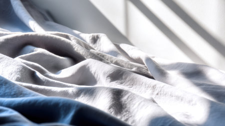 A serene close-up of soft, wrinkled fabric in shades of blue and white, illuminated by sunlight, creating gentle shadows and a calming atmosphere for any room.の素材