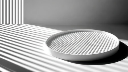 A minimalist flat circular tray sits on a soft gray surface, surrounded by striking shadows and light patterns from vertical stripes, creating an elegant atmosphere.の素材