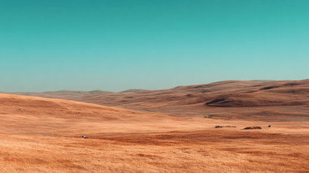 A breathtaking view of a golden prairie landscape under a clear turquoise sky. The rolling hills create a serene and expansive natural setting ideal for outdoor enthusiasts.の素材