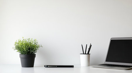 A contemporary office desk with a laptop, plant, and pens, set against a clean white wall, leaving plenty of space for copy.の素材