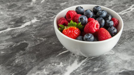 A bowl of fresh mixed berries, including strawberries, blueberries, and raspberries, on a marble surface with space for design.の素材
