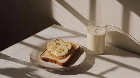A table setting with toast, peanut butter, banana slices, and a glass of milk, arranged with natural lighting.の素材