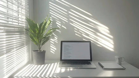 A minimalist setup with a laptop on a white desk, showing an open, empty document, complemented by a notebook and a stylish plant.の素材
