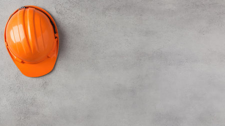 Flat lay of a bright orange hard hat on a smooth, gray industrial surface.の素材