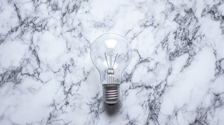 A minimalistic photo of a light bulb lying flat on a marble surface under soft lighting.の素材