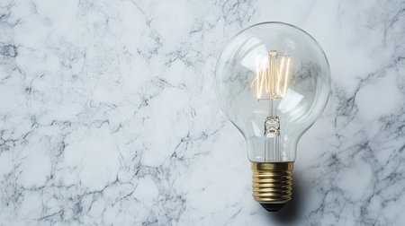 A minimalistic photo of a light bulb lying flat on a marble surface under soft lighting.の素材