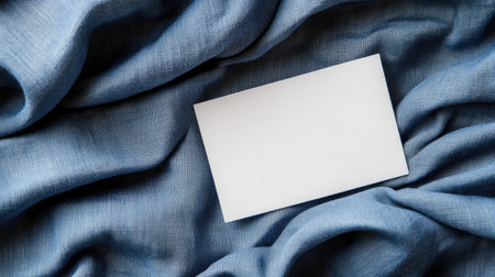 Blank white business card on a smooth blue fabric texture background with subtle folds.の素材