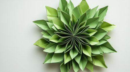 A symmetrical origami flower with intricate folds in shades of green, positioned in the center of a light-colored background.の素材
