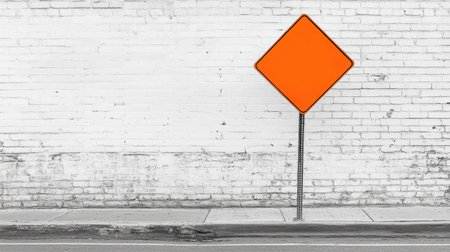 A bright orange construction road sign placed on a deserted street, with plenty of copy space around it.の素材