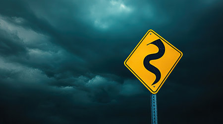 A yellow road warning sign with a symbol indicating slippery road conditions, set against a dark sky with copy space.の素材