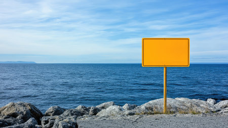 A blank yellow road hazard sign standing near a rocky cliff edge, offering plenty of copy space with a vast sky and ocean view behind.の素材