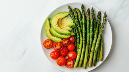 A heart-healthy plate of grilled asparagus, cherry tomatoes, and avocado slices on a light marble background.の素材