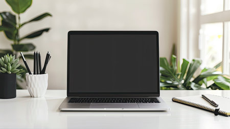 Mockup of a laptop screen on a clean, white desk with a notepad and penの素材