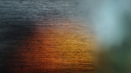 This abstract image captures the beauty of a brushed metal surface featuring warm orange light and a soft-focused background, showcasing unique textures and reflections.の素材