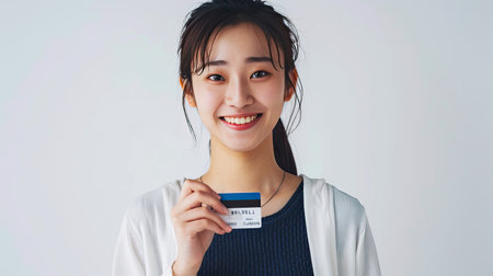 Young Asian woman with a credit card, smiling and pointing for online transactions. Isolated on whiteの素材