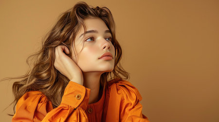 Portrait of a thoughtful woman wearing chic orange clothes, isolated on khakiの素材
