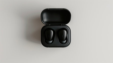 Top view of compact black earbuds in charging case, isolated against a white background for tech accessory conceptsの素材