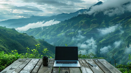 Scenic laptop setup on wooden deck with lush green mountains and misty clouds, ideal for nature loversの素材