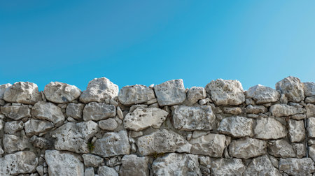 Grunge stone wall with rough, uneven textures, and a serene blue sky in the backgroundの素材