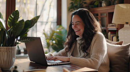 Happy mature woman smiling while using a laptop at a cozy living room table, natural light from windowsの素材