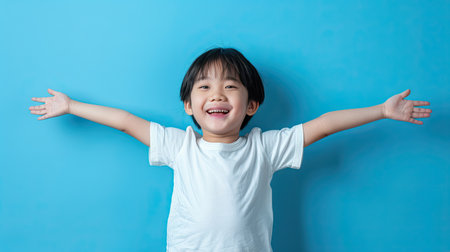Happy Asian child posing with arms outstretched on a blue backdrop, emphasizing enthusiasm and joyの素材