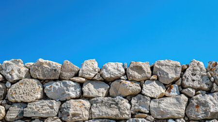 Stone wall with detailed, natural textures and a clear blue sky, ideal for background or texture referenceの素材