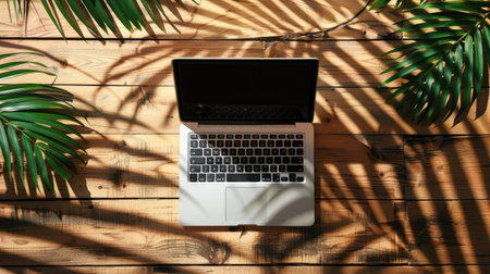 Top view of a laptop with a blank screen on a wooden background, with shadows from palm leaves. Perfect for digital summer and tropical themes.の素材