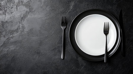 Close-up of a clean plate and cutlery arranged on a black table, showcasing a simple and elegant setup with ample space for your messageの素材